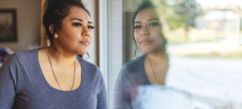 Woman looking outside through window, with her reflection showing. 